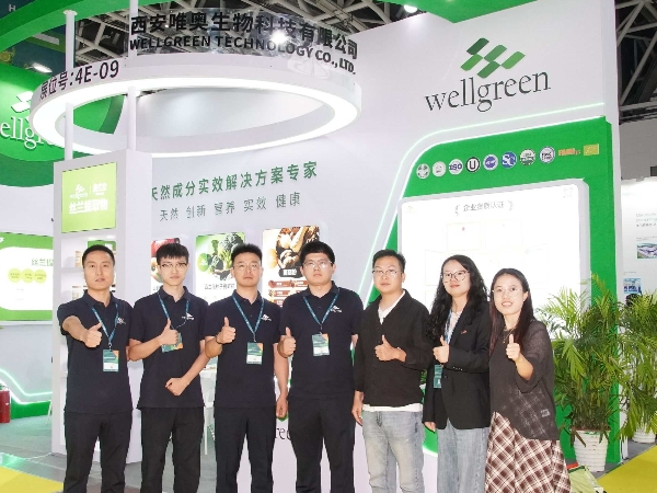 Smiling team posing in front of a modern green-themed botanical extract exhibit booth